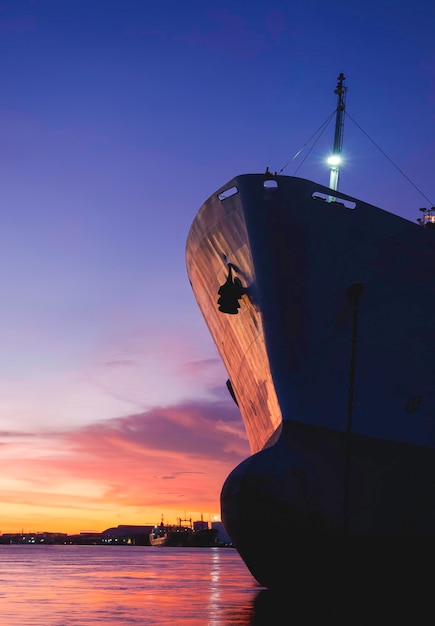 Silhouette oil tanker ship moored at harbor against colorful sunset sky background in evening time