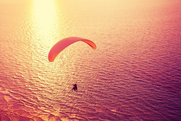 Silhouette di parapendio che sorvola il mare al tramonto