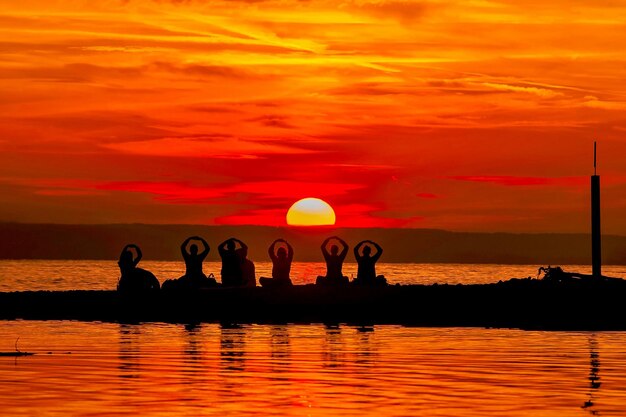 Silhouette people on at beach against sea and sky during sunset