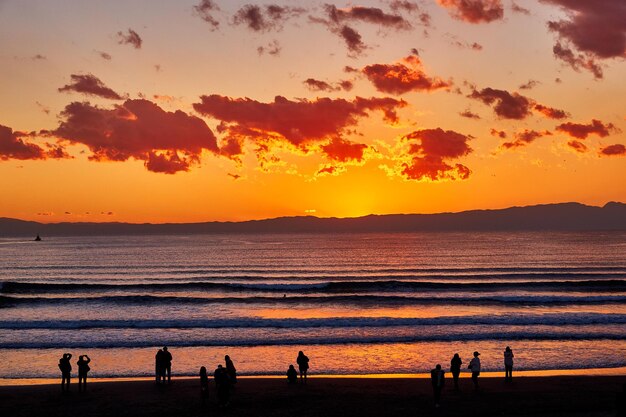 Silhouette people on beach against sky during sunset