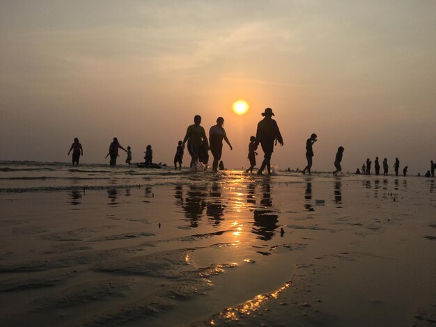 Photo silhouette people at beach against sky during sunset