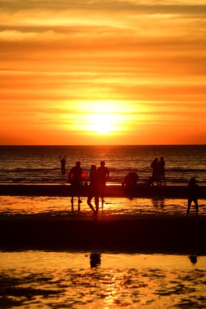 Silhouette people on beach against sky during sunset