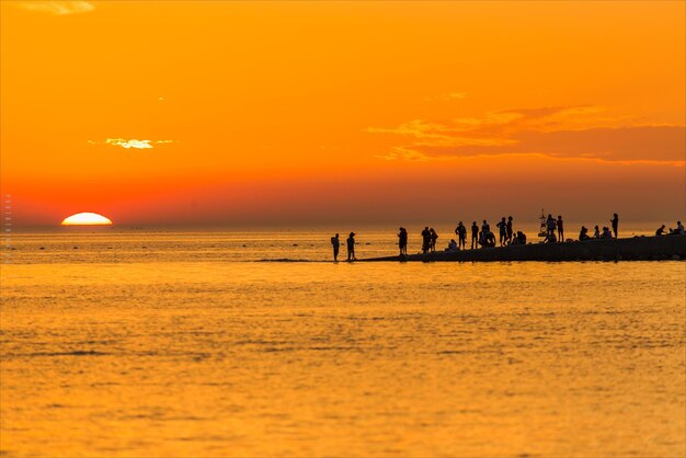 Silhouette people on beach against sky during sunset