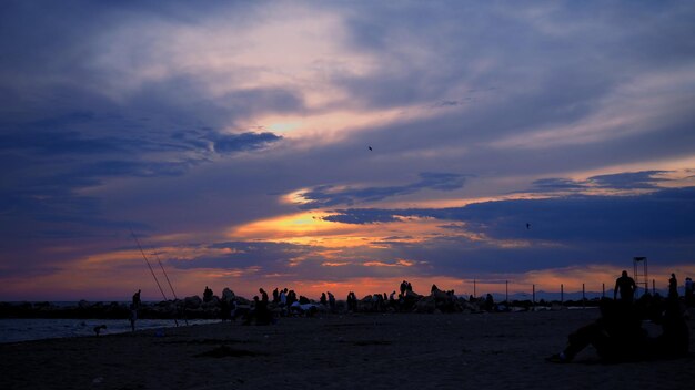 Silhouette people on beach against sky during sunset