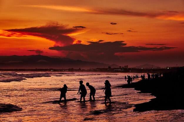 Silhouette people on beach against sky during sunset