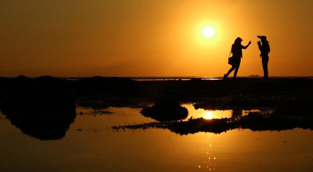 Photo silhouette people by sea against sky during sunset