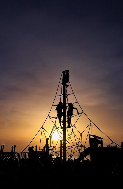 Silhouette people climbing jungle gym against cloudy sky during sunset