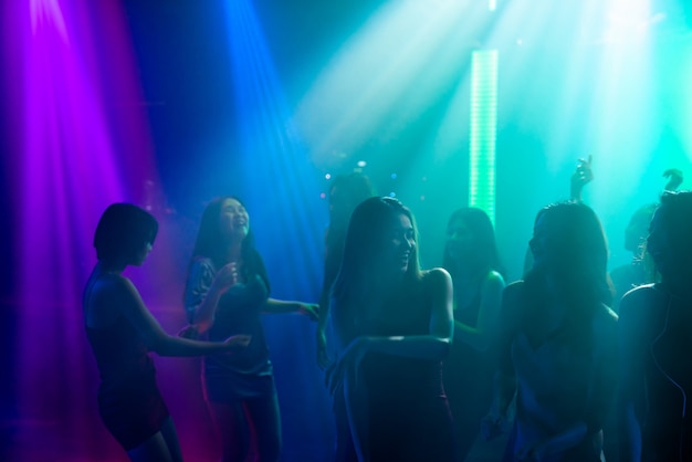 Silhouette di persone ballano in discoteca night club alla musica di dj sul palco