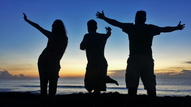 Foto silhouette di persone che si godono la spiaggia durante il tramonto