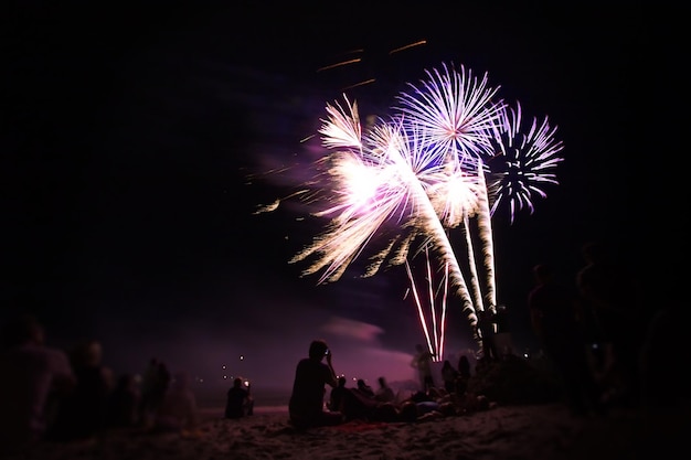 silhouette people enjoying firework display from beach at night
