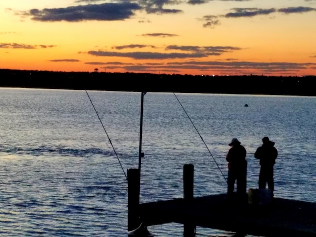 夕暮れの空に反して海で釣りをしている人々のシルエット