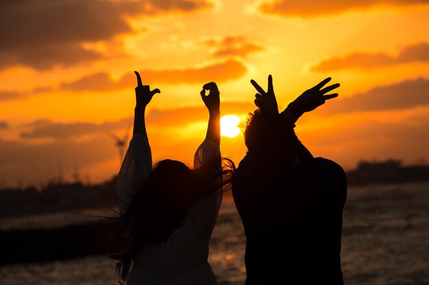 Silhouette people gesturing at beach during sunset