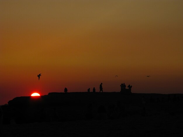 Silhouette people on land against orange sky during sunset