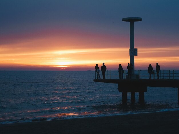 写真 夕暮れの空を背景にビーチに立つ人々のシルエット