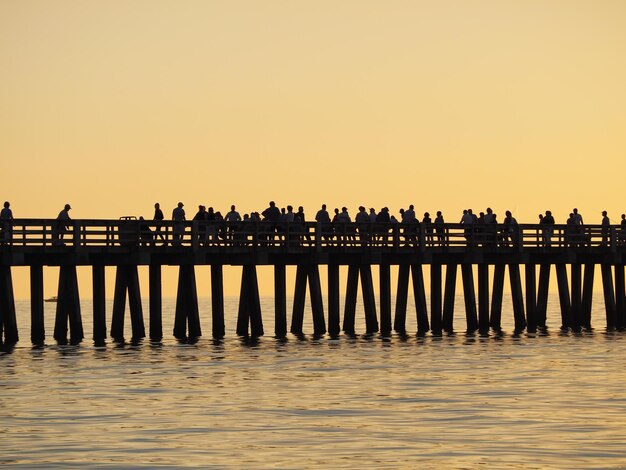 Foto silhouette di persone sul molo sopra il mare contro un cielo limpido durante il tramonto