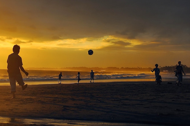 Photo silhouette of people playing on beach at sunset