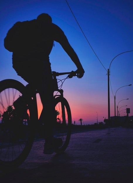 Фото Силуэт людей, едущих на велосипеде по улице напротив неба во время захода солнца