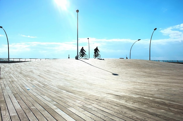 Foto silhouette di persone in bicicletta su una passeggiata contro il cielo blu durante una giornata di sole