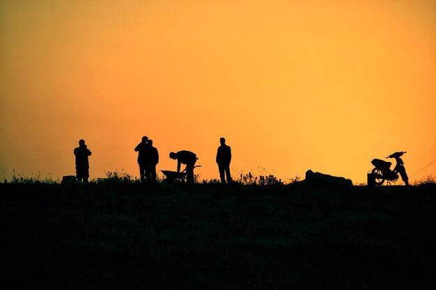 Silhouette people riding on field against sky during sunset