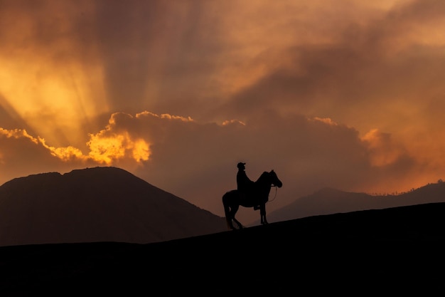 Silhouette people riding horse on mountain during sunset