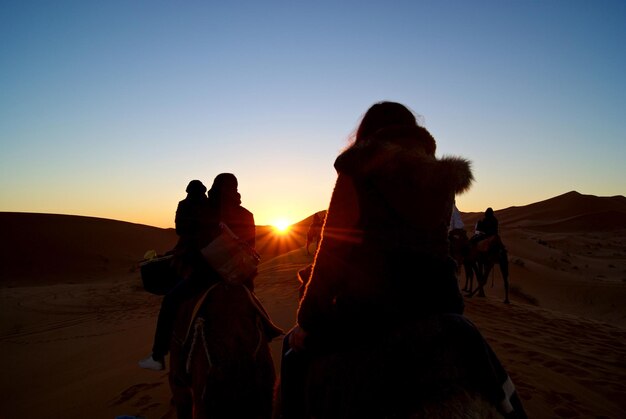 写真 夕暮れの空に逆らって砂漠に乗っているシルエットの人々