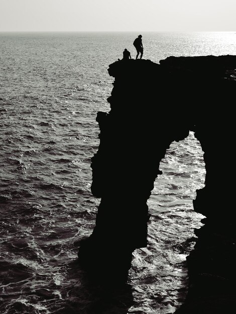 Photo silhouette people on rock formation at beach against sky