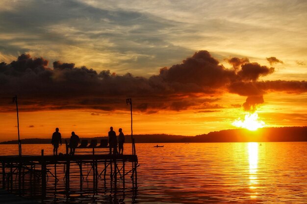 Silhouette people on sea against sky during sunset