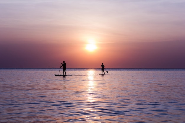 夕暮れの空を背景に海に描かれた人々のシルエット