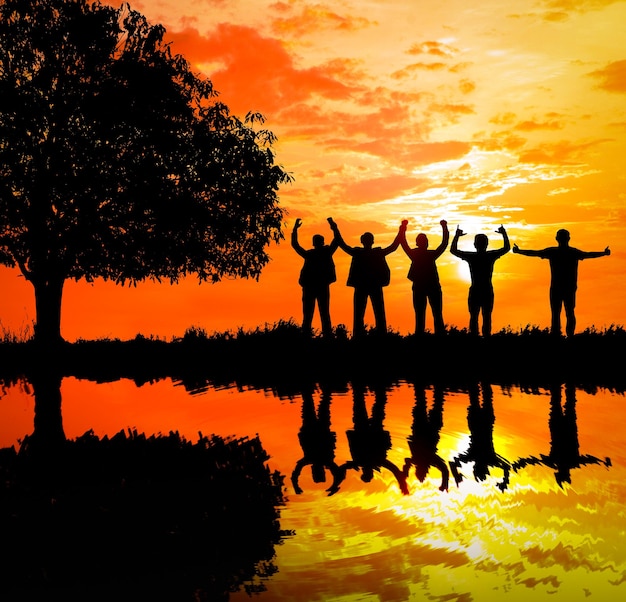 Photo silhouette people standing by lake against orange sky