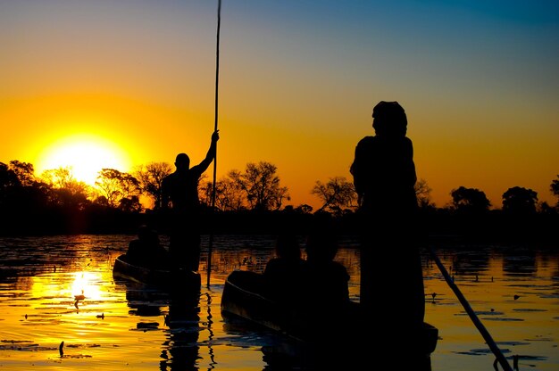 Silhouette people standing by lake against sky during sunset