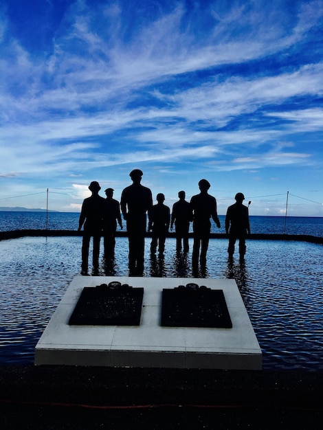 Silhouette people standing by sea against sky