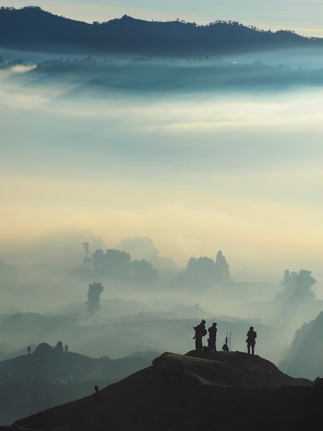 Photo silhouette people standing on mountain during foggy weather