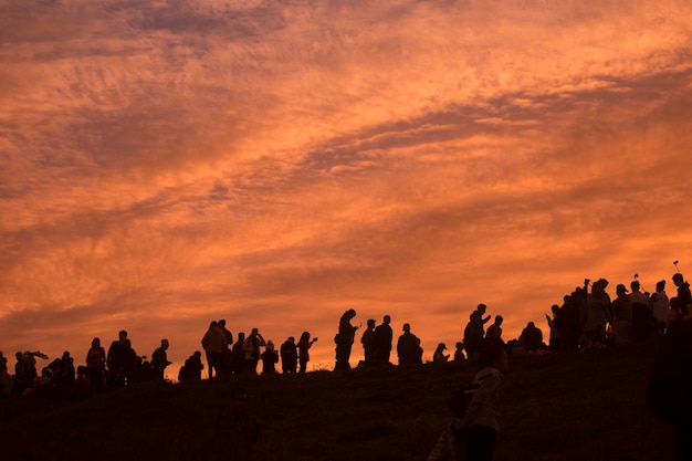 写真 夕暮れの間雲の空を背景に山の上に立っているシルエットの人々