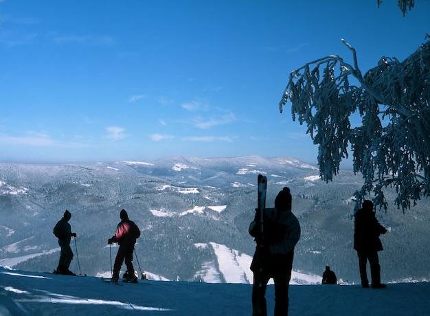 写真 空に向かって雪に覆われた山の上に立っているシルエットの人々