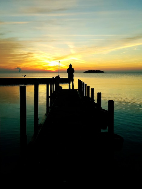 Photo silhouette of people standing on pier at sunset