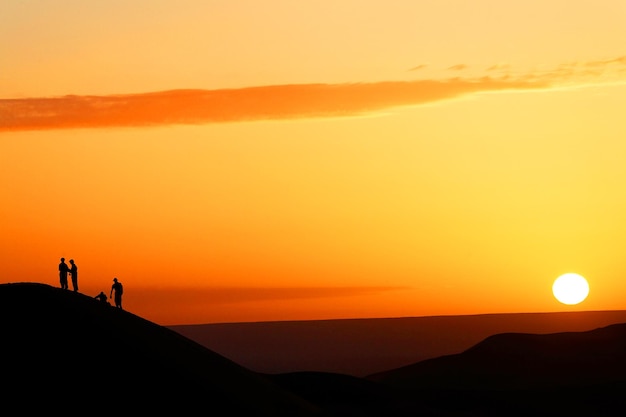 Silhouette people standing on sand dune at erg chebbi desert against sky during sunset