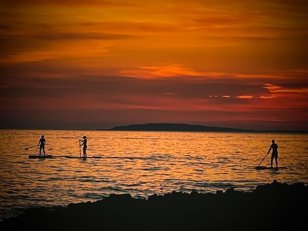 Silhouette people standing on sea against sky during sunset