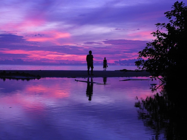 Silhouette people standing on shore against sky during sunset