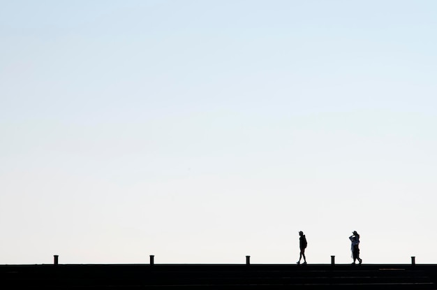 Silhouette people walking on bridge against clear sky