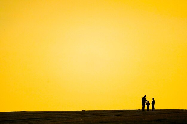 Photo silhouette people walking on fields against orange sky