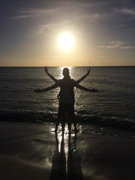 Foto silhouette di persone con le braccia tese in piedi sulla riva del mare durante il tramonto