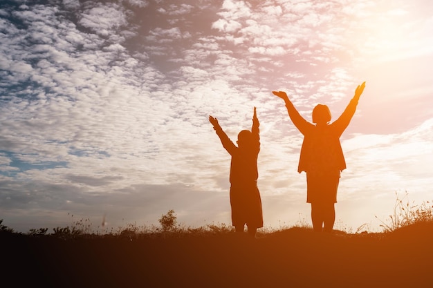 silhouette people with arms raised standing on land against sky during sunset
