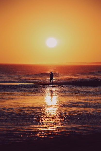 Photo silhouette person on beach against sky during sunset