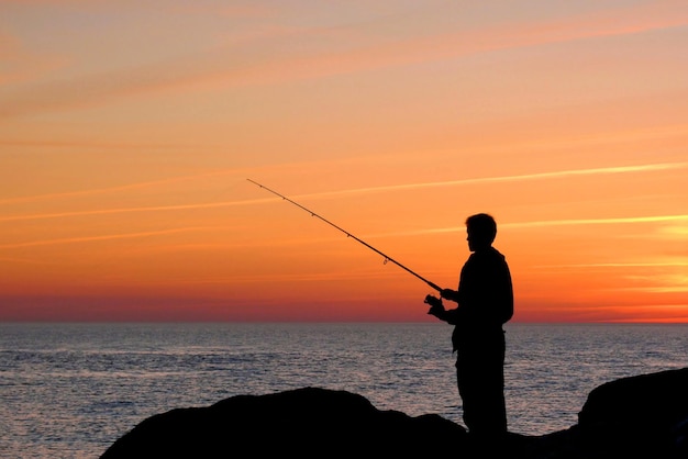 silhouette of person fishing at sunset