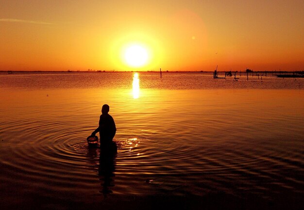 Silhouette person at lake against sky during sunset