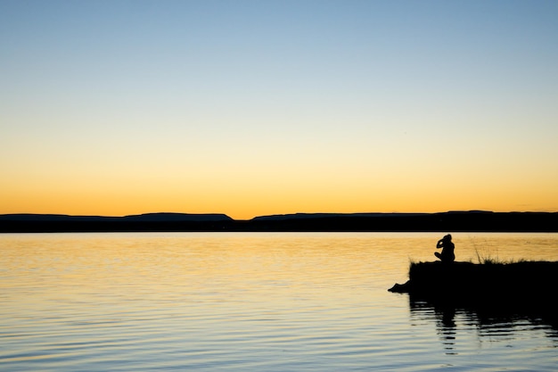 夕暮れの晴れた空を背景に湖岸のシルエットの人