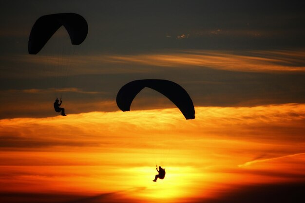 Silhouette person paragliding against sky during sunset