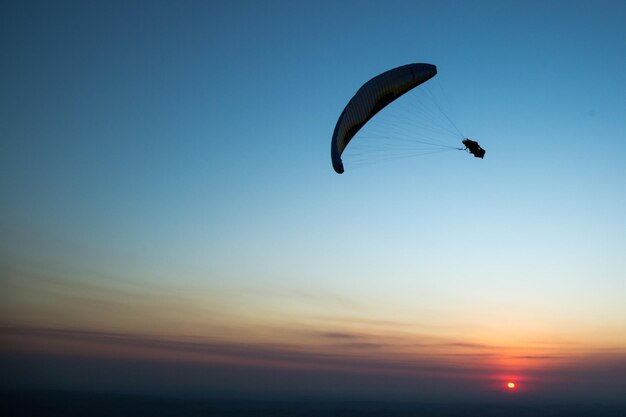 夕暮れの空に向かってパラグライディングするシルエットの人