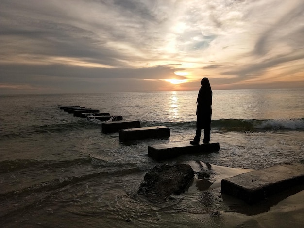 夕暮れの空を背景にビーチの岩の上に描かれたシルエット