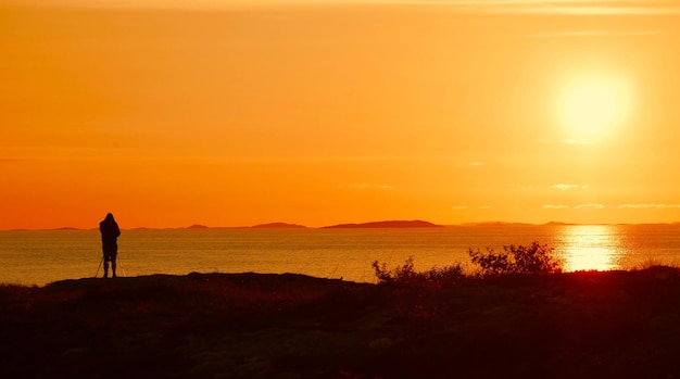 Silhouette person standing at beach against sky during sunset